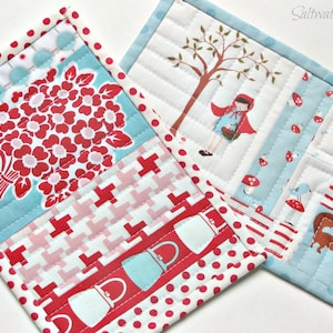 May include: Two rectangular quilted fabric mats featuring patchwork designs. One mat displays a red floral bouquet, red and white geometric patterns, and red polka dots. The other mat depicts a character in a red hood, a tree, and a fox.