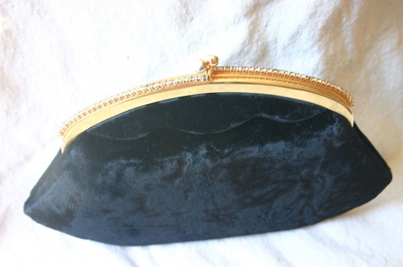 Peut inclure: Un sac de soir&eacute;e en velours noir avec une fermeture en m&eacute;tal dor&eacute; et une bordure perl&eacute;e.