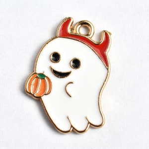 May include: A gold-tone metal charm featuring a white ghost with red devil horns holding a small orange pumpkin. The ghost has black eyes and a smiling mouth.