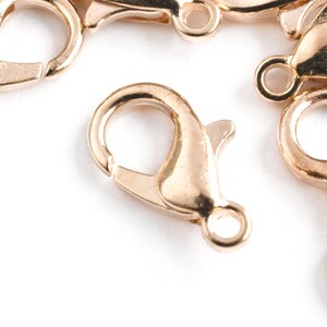 May include: Close-up of several gold-colored lobster claw clasps. These clasps are used for jewelry making and feature a spring-loaded mechanism for secure closure. The clasps are made of a shiny, metallic material and are set against a white background.