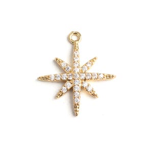 May include: A gold-colored star charm with eight pointed rays. Each ray and the center of the star are encrusted with small, clear crystals. The charm has a small loop at the top for attaching to a necklace or bracelet.