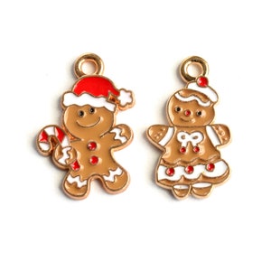 May include: Two gold-colored gingerbread person charms with white icing and red accents. The gingerbread person on the left is holding a candy cane. The gingerbread person on the right is wearing a white hat.