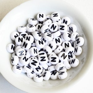 May include: A white bowl filled with white round beads with the letter "N" printed in black on each bead.