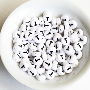 May include: A white bowl filled with white round beads with the letter "T" printed in black on each bead.