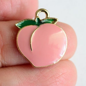 May include: Gold-tone peach charm with a green leaf. The peach is pink and has a gold outline.