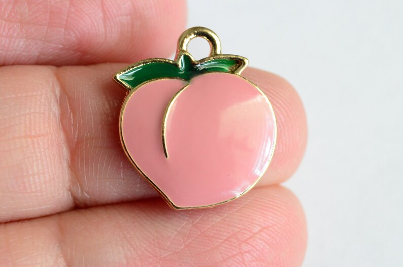 May include: Gold-tone peach charm with a green leaf. The peach is pink and has a gold outline.