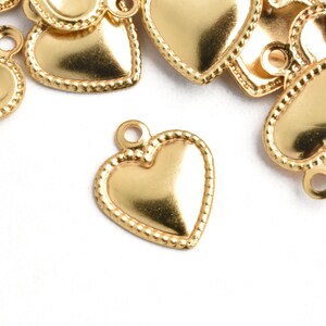 May include: A group of gold heart-shaped charms with a beaded edge. The charms have a loop at the top for attaching to jewelry or other crafts.
