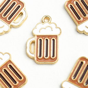 May include: Five gold-colored metal charms shaped like beer mugs with white foam tops. The mugs have brown and black details.