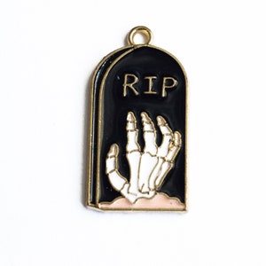 May include: Gold-tone metal charm shaped like a black tombstone with a white skeleton hand reaching out from the ground. The tombstone has the inscription "RIP" on it.