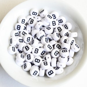 May include: A white bowl filled with white plastic letter beads, all with the letter "B" printed in black.