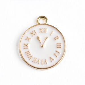 May include: A gold-colored metal clock charm with a white face and gold Roman numerals. The clock hands point to approximately 5 o'clock. The charm has a small loop at the top for attaching to a necklace or bracelet.