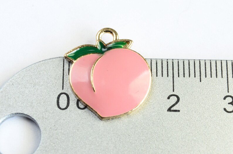 May include: Gold-tone peach charm with a green leaf, measuring approximately 1 inch in diameter. The charm is pink and has a shiny finish.