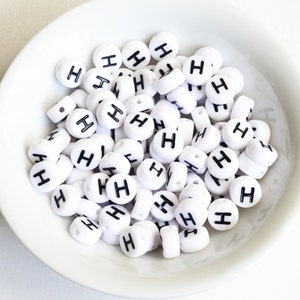 May include: A white bowl filled with white round beads with the letter "H" printed in black on each bead.
