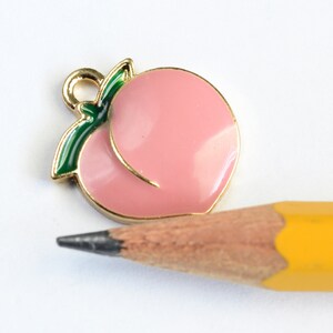May include: Gold-toned peach charm with a green leaf, perfect for adding a touch of fruit-inspired style to jewelry or crafts.