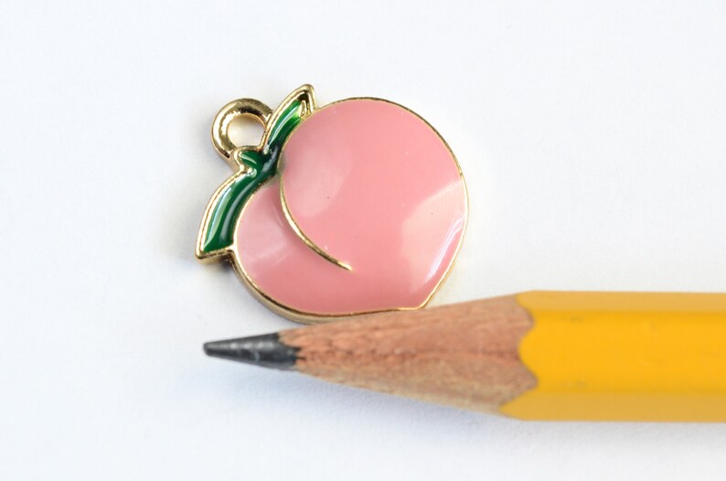 May include: Gold-toned peach charm with a green leaf, perfect for adding a touch of fruit-inspired style to jewelry or crafts.