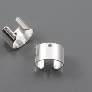 May include: Two silver metal rings with a rounded shape. One ring has a small hole on the top.