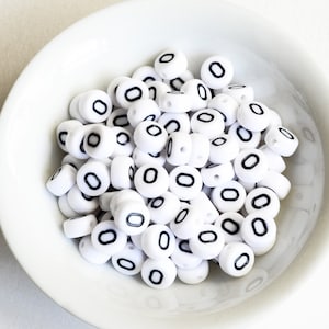 May include: A white bowl filled with white plastic beads with black numbers "0" printed on them.