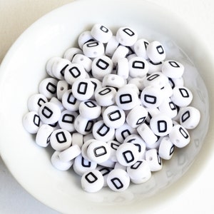 May include: A white bowl filled with white plastic beads with black letter "O" printed on each bead.
