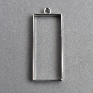 May include: Silver-toned metal pendant with a rectangular frame. The frame is open on all sides and has a loop at the top for hanging.