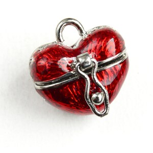 May include: A small, red heart-shaped locket with a silver hinged lid and a silver chain. The locket is a charm or pendant.