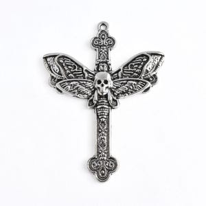 May include: A silver-toned metal pendant shaped like a cross with an ornate, textured surface. The center features a detailed human skull flanked by two large, spread insect wings. A small circular loop is attached to the top for hanging.