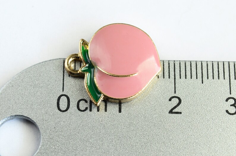 May include: Gold-tone peach charm with a green leaf, measuring approximately 1 cm in length.