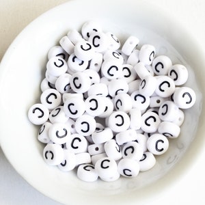 May include: A bowl filled with white plastic letter beads, each bead has the letter "C" printed in black.