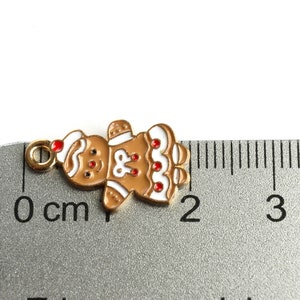 Może przedstawiać: Zawieszka w kształcie piernikowego ludzika z białą polewą i czerwonymi akcentami z cukierk&oacute;w. Zawieszka ma około 1,5 cm wysokości i ma złotą pętelkę do zawieszenia.