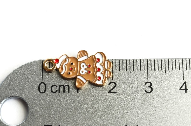 Może przedstawiać: Zawieszka w kształcie piernikowego ludzika z białą polewą i czerwonymi akcentami z cukierk&oacute;w. Zawieszka ma około 1,5 cm wysokości i ma złotą pętelkę do zawieszenia.