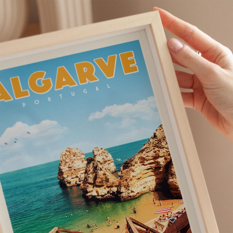 A person's hand is holding a framed picture of a scenic coastal landscape in Portugal, featuring rocky cliffs, a beach, and a clear blue sky.