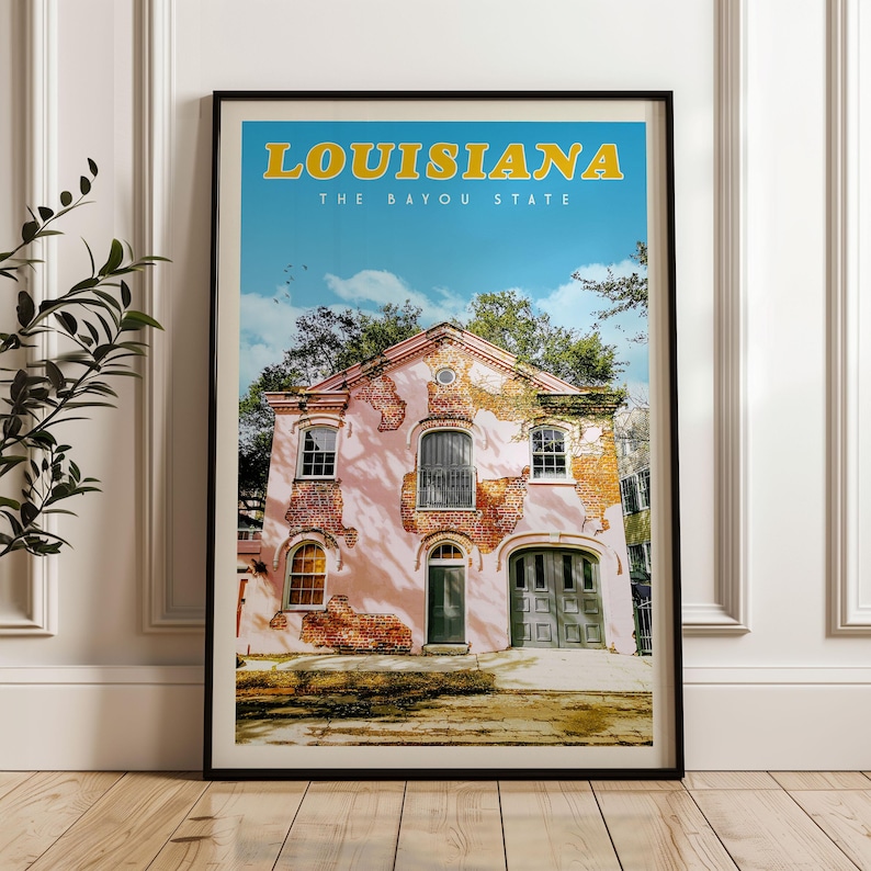 A framed poster of a pink building with a green door and windows, set against a blue sky with trees, in the state of Louisiana.
