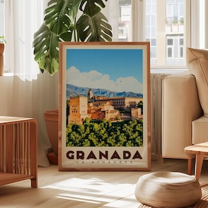 A framed poster of Granada, the capital city of Alhambra, Spain, is displayed in a living room setting with a potted plant and a sofa visible in the background.