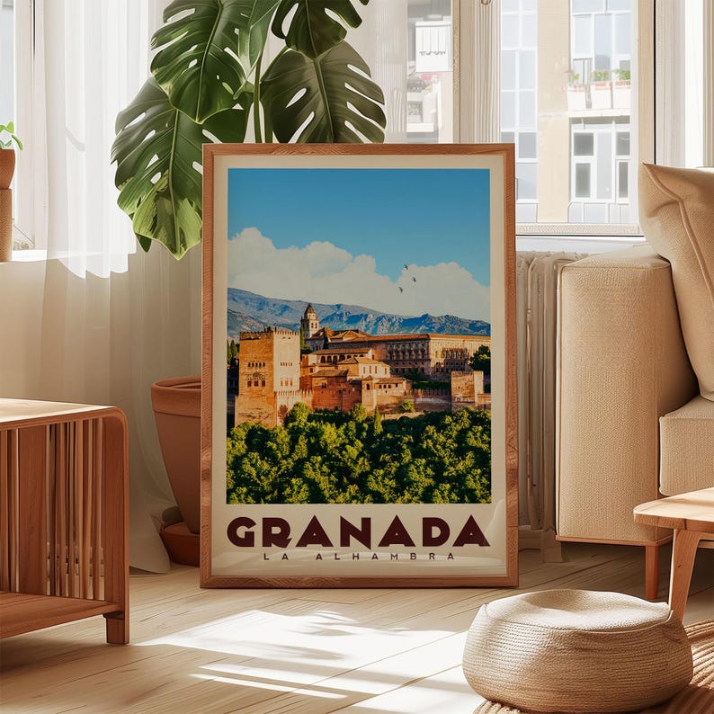 A framed poster of Granada, the capital city of Alhambra, Spain, is displayed in a living room setting with a potted plant and a sofa visible in the background.
