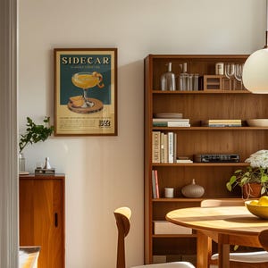a cozy living room with a wooden bookshelf, a framed poster of a cocktail, and a wooden cabinet. The room has a warm and inviting atmosphere, with natural light streaming in from the window.