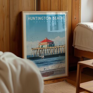 A framed poster of Huntington Beach, California, featuring a red-roofed pier with a building and a person on the water.