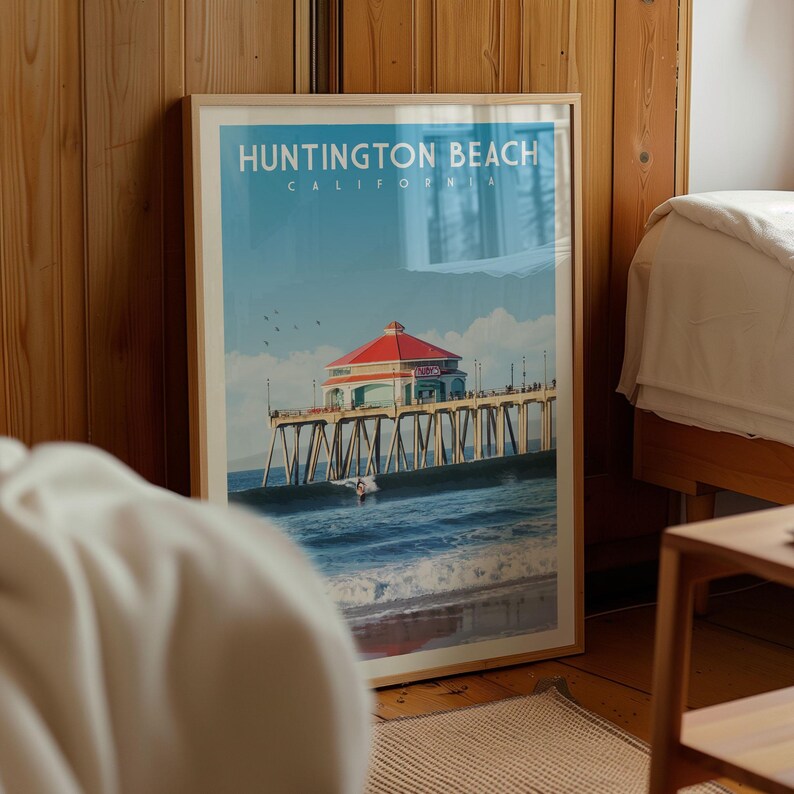 A framed poster of Huntington Beach, California, featuring a red-roofed pier with a building and a person on the water.