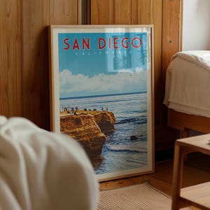A framed poster of a scenic coastal landscape with cliffs and people enjoying the view, displayed in a room with wooden walls.