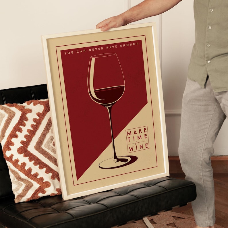 A person is holding up a framed poster with a wine glass illustration and the text "You can never have enough" and "Make time for wine" on it.