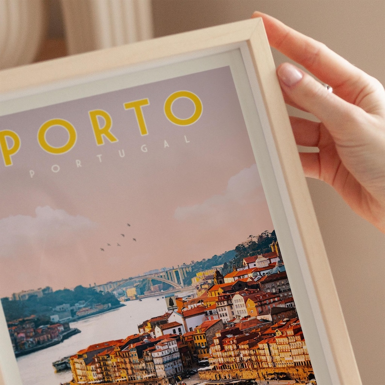 A person's hand is holding a framed poster of the city of Porto, Portugal, with a colorful and detailed view of the city's skyline and river.