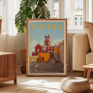 a framed poster of a colorful cityscape with a clock tower, displayed in a living room setting with a large window and a potted plant.