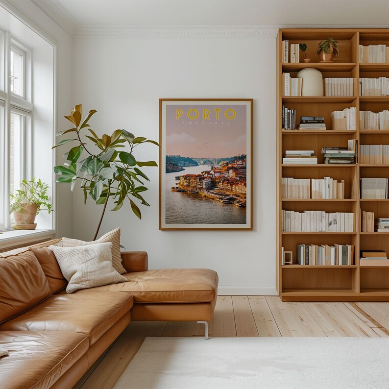 a cozy living room with a large window, a comfortable leather couch, a bookshelf filled with books, and a framed poster of a scenic view of Porto, Portugal.