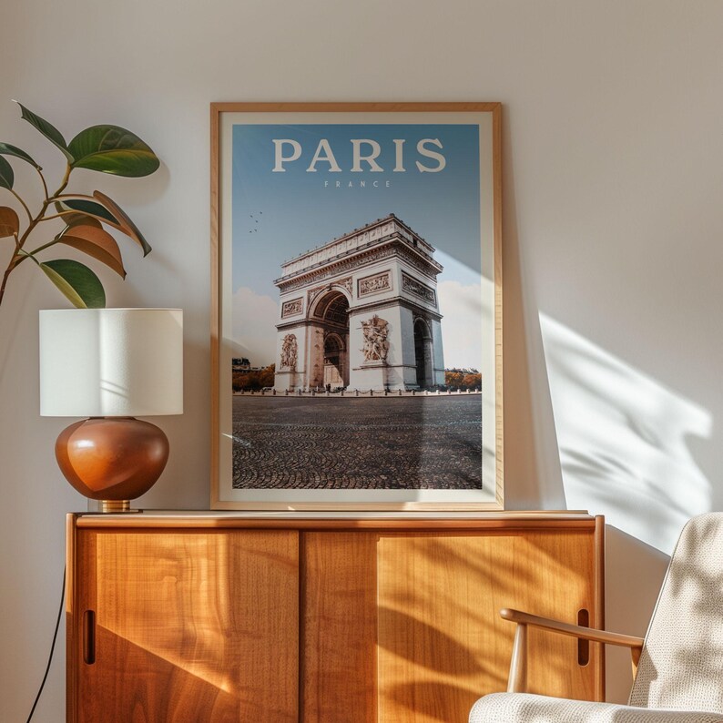 a framed poster of the Arc de Triomphe in Paris, France, hanging on a wall next to a wooden cabinet and a lamp.