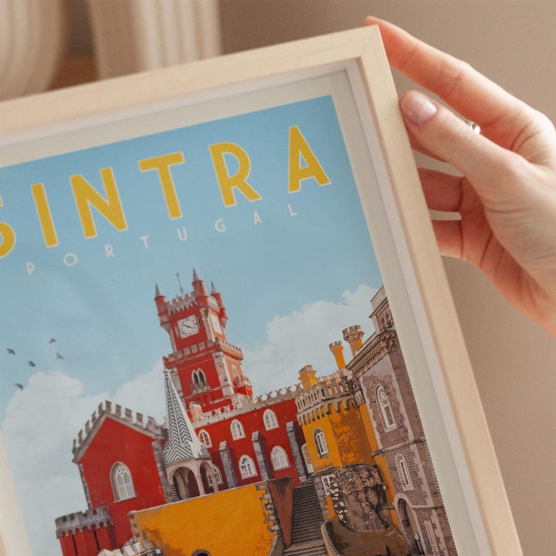 A person's hand is holding a framed poster of the Sintra city in Portugal, featuring a colorful illustration of the city's architecture and landmarks.