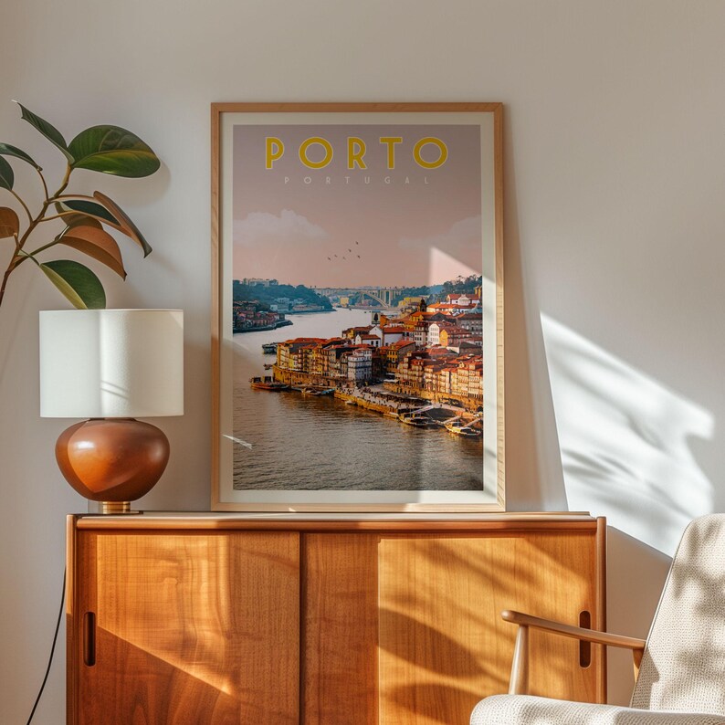 a framed poster of the city of Porto, Portugal, hanging on a wall next to a wooden cabinet and a lamp.
