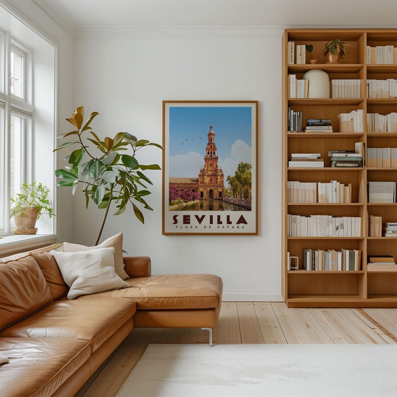 a cozy living room with a large bookshelf filled with books, a comfortable leather couch, and a framed poster of a building with a bell tower, which is the Seville, Spain landmark.