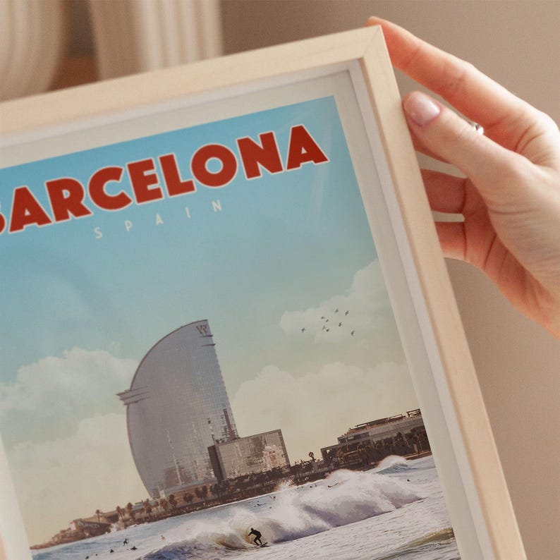 A person's hand is holding a framed picture of a cityscape with a large building and a surfer in the foreground.