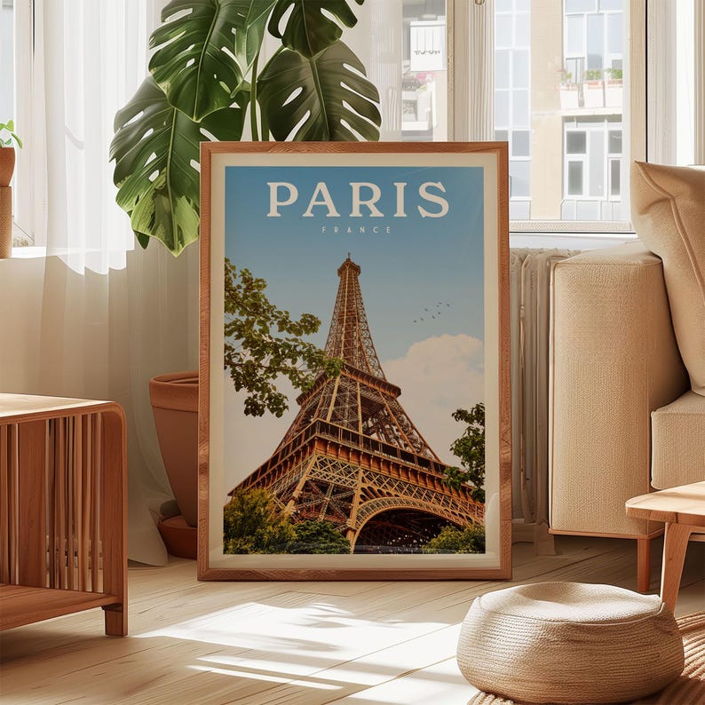 A framed poster of the Eiffel Tower in Paris, France, is displayed in a living room setting with a large window and a potted plant in the background.