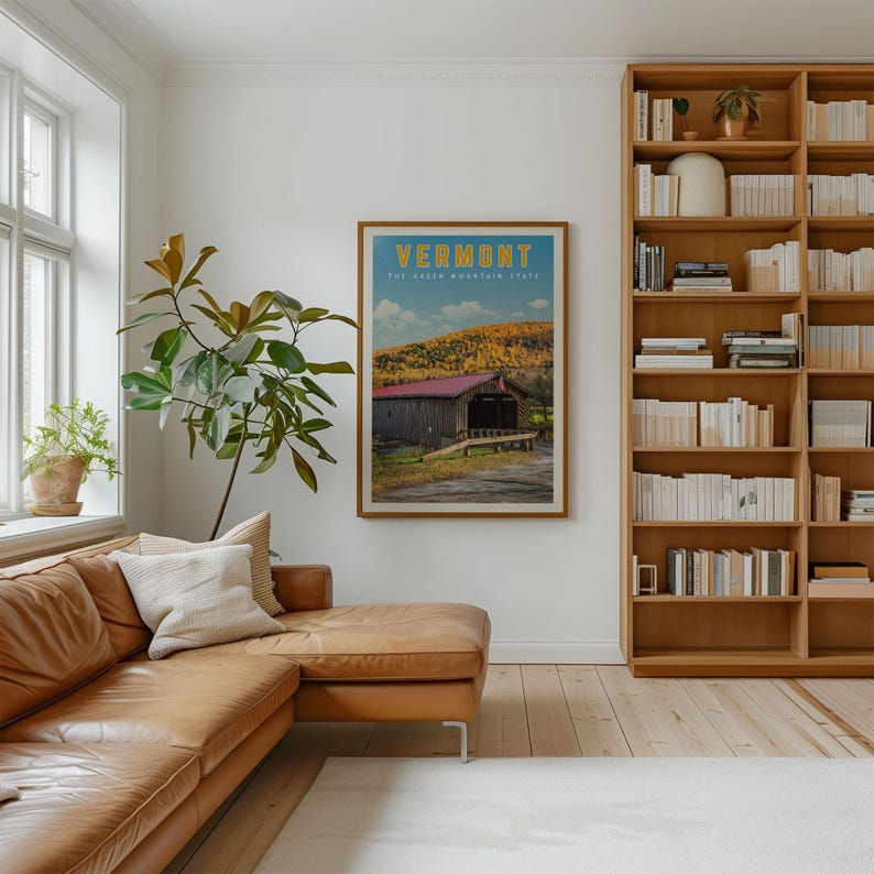 a cozy living room with a brown leather sofa, a large bookshelf filled with books, and a framed poster of a scenic mountain landscape hanging on the wall.