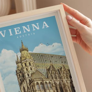 A person's hand is holding a framed poster of the St. Peter's Basilica in Vienna, Austria.