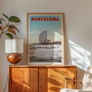 a framed poster of Barcelona, Spain, hanging on a wall above a wooden cabinet.